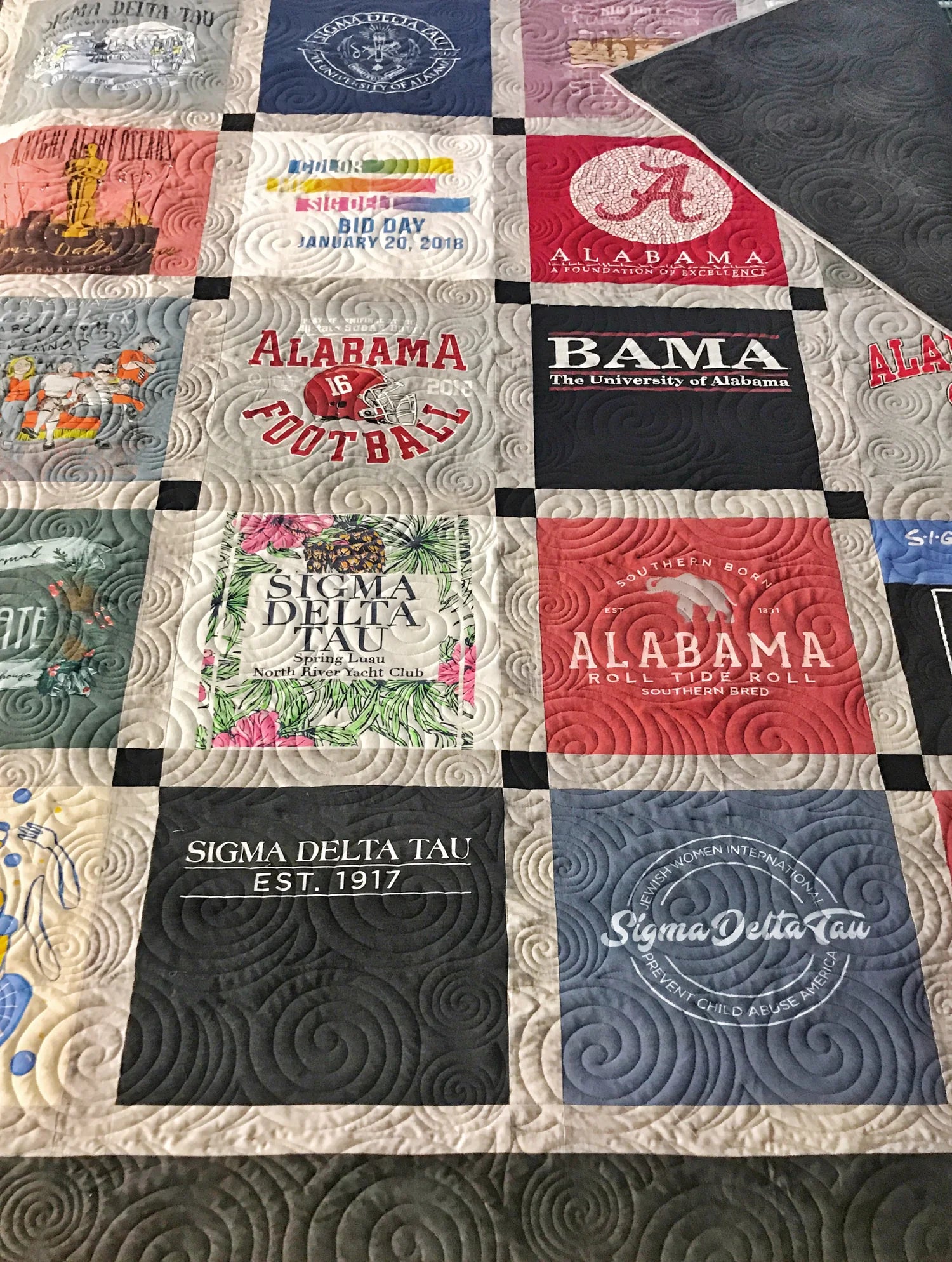 Quilt with patches featuring various logos and text, including 'Alabama' and 'Sigma Delta Tau'.